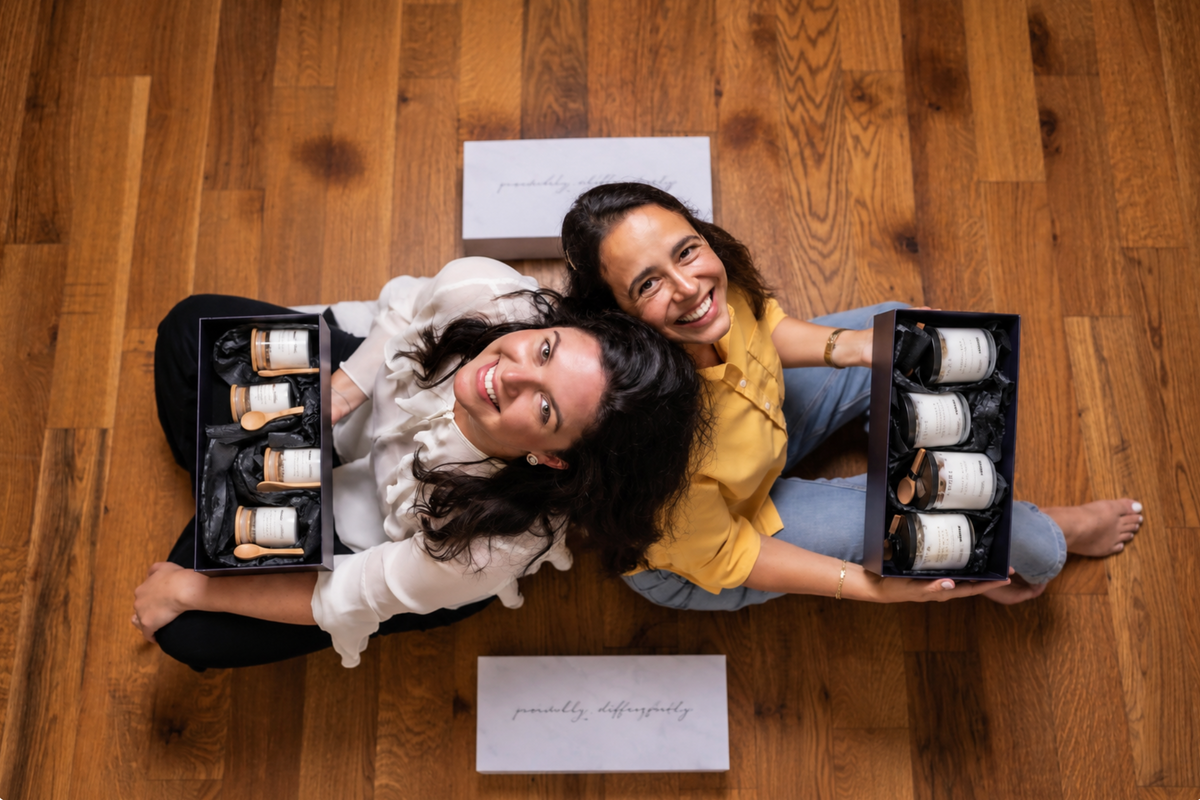 Two women holding open black gift boxes, each containing four Incanto candles