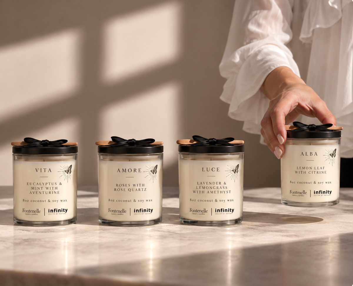 Four 8 oz Incanto candles in Vita, Amore, Luce and Alba on a marble surface, with a hand lifting Alba