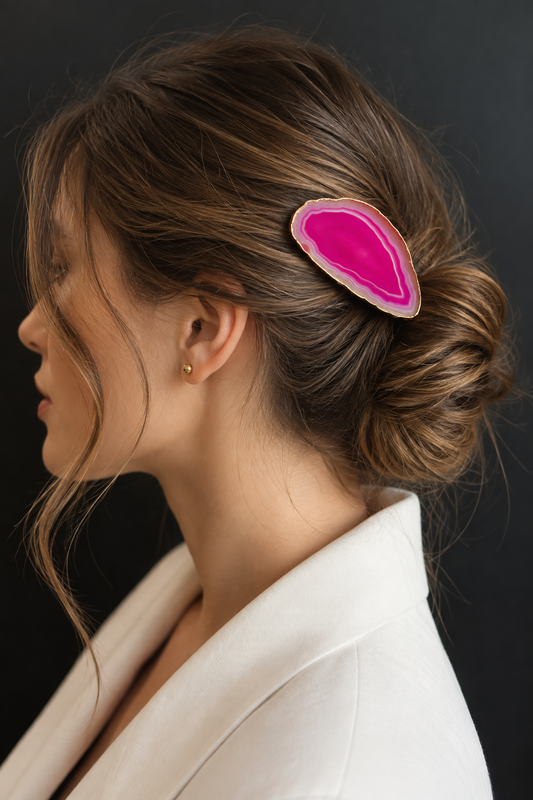 A woman in profile wearing a bright pink teardrop-shaped hair clip with a natural agate stone edge, styled in a low bun.